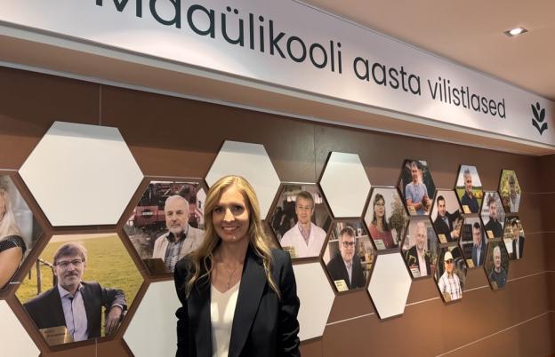 Naine seisab seina ääres, taamal inimeste pildid