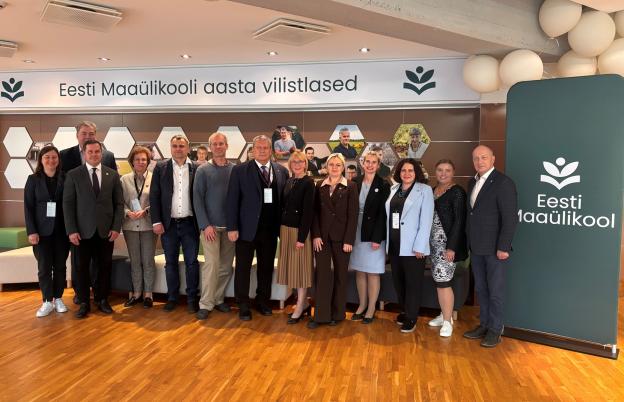 Inimeste grupipilt siseruumides, taga seinal portreefotod