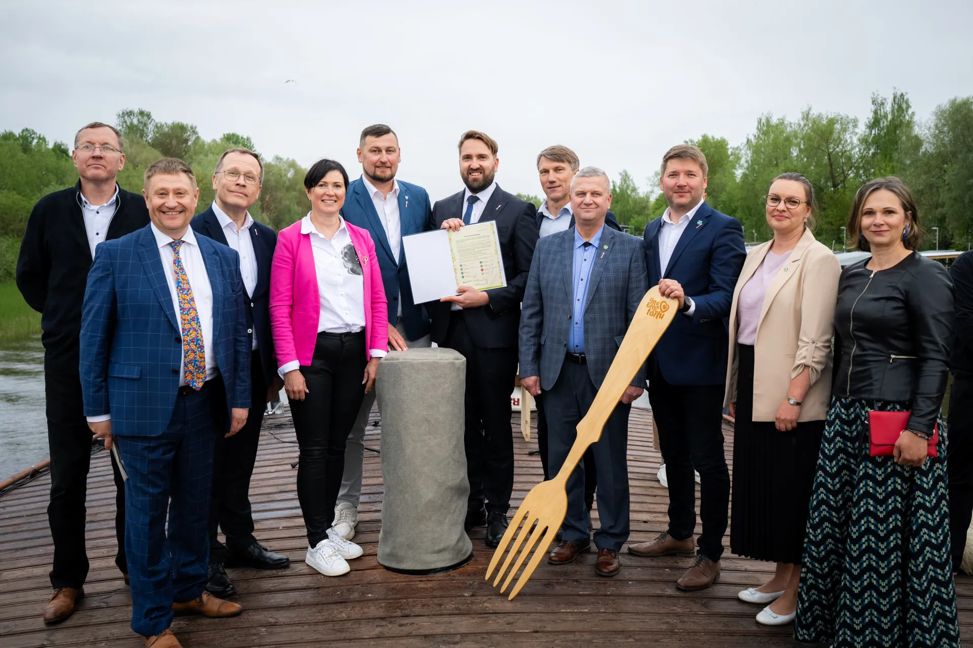 Grupp inimesi seisab õues ja näitab fotograafile allkirjastatud dokumenti