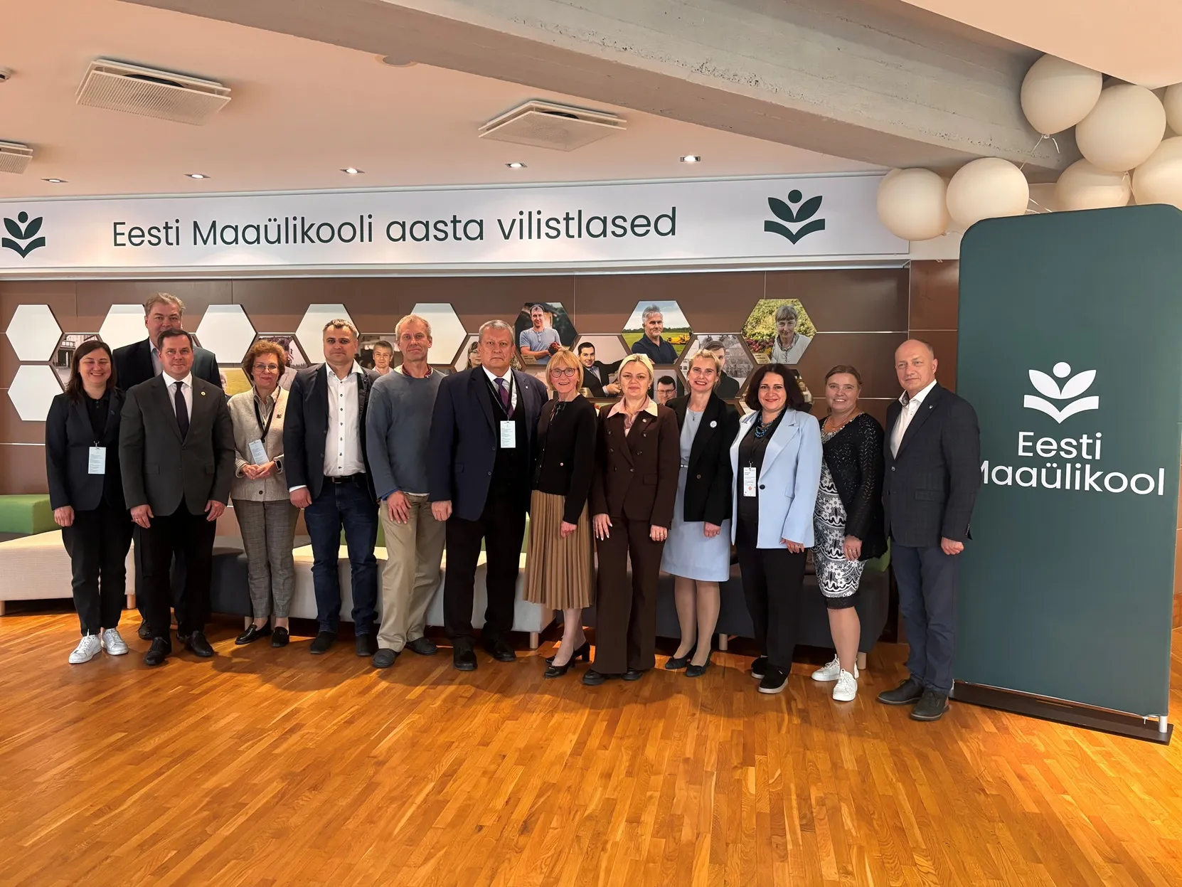 Inimeste grupipilt siseruumides, taga seinal portreefotod